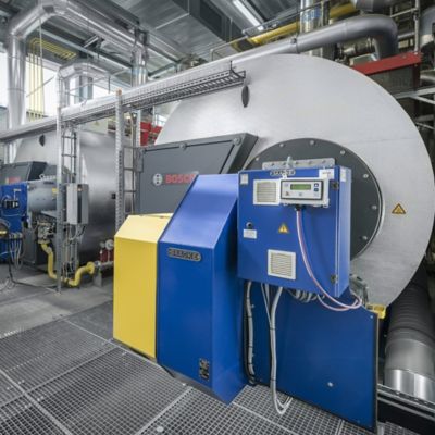 An industrial boiler room with 2 Bosch hot water boilers UT-H and yellow and blue control panels.