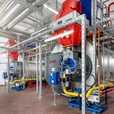 An industrial setting with multiple Bosch steam boilers, connected with intricate piping and visible red and blue control units for optimized operation.