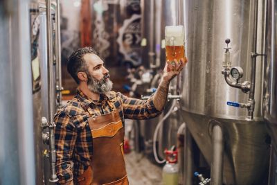 Image of a brewer looking a a mug of beer in a brewery with stainless steel tanks