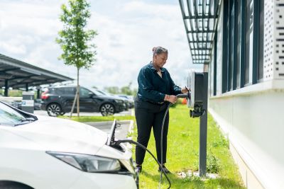 A woman at an EV car charging station plugging in the charger. 