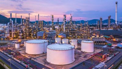 A chemical plant at night, with large white chemical tanks in front of an oil refinery