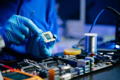 Technician with gloves installs CPU on motherboard using tools. 