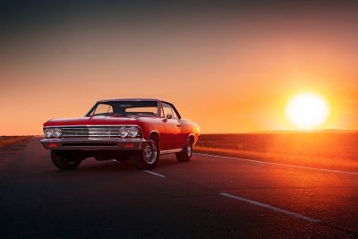 A classic car sits on a large, empty road at sunset