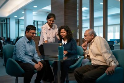 Colleagues gathered around a laptop in an office sitting area.