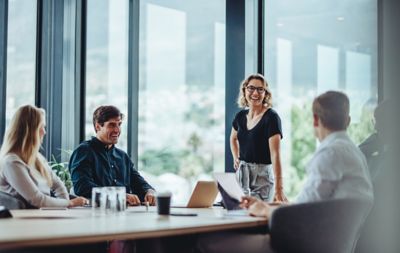 Office colleagues having casual discussion during meeting in conference room. Group of men and women sitting in conference room and smiling.