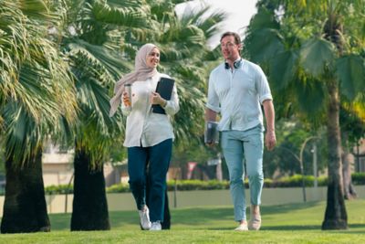 Two colleagues with laptops walking across lawn