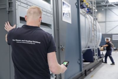 Two Eco Steam and Heating Solutions technicians moving a large industrial boiler in a warehouse setting. 