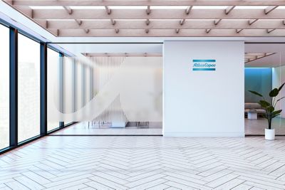 Open office space with an Atlas Copco logo wallpaper in a cutout shape on a glass wall