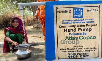 A girl sitting on the ground next to a hand pump decorated with the project's promotional banner.