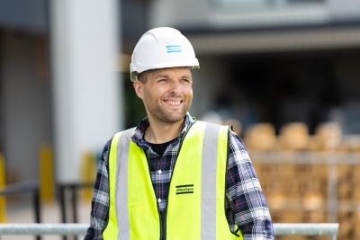 Man smiling wearing a helmet and a yellow jacket branded atlas copco 