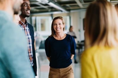 A group of male and female colleagues are standing in a circle having a conversation with smiles on their faces. ​