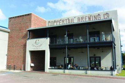 A front view of the Coppertail Brewing Company location, with two-story patio seating and a brick wall