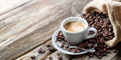 A white coffee cup with hot coffee, on a saucer with spilled coffee beans