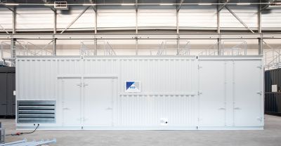 A custom-built white container with secured doors, ventilation grilles, and external pipe connections. The unit features a visible "eco" logo and is placed in a clean industrial environment with overhead lighting and structural frameworks in the background.