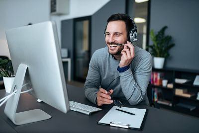 A man wearing a headset smiles while looking at his computer screen