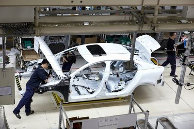 Car manufacturing in China, operator working on half-built car. 