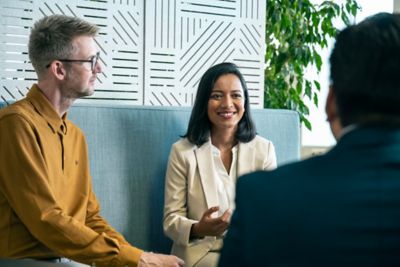 One woman and two men are sitting in an office having a happy conversation. ​