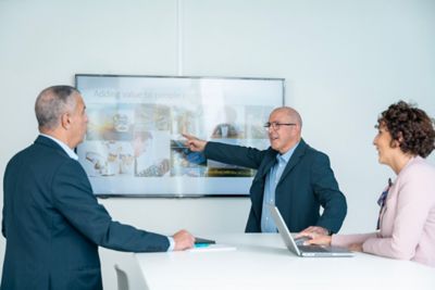 Three executives at a standup meeting with team leader pointing at the whiteboard.