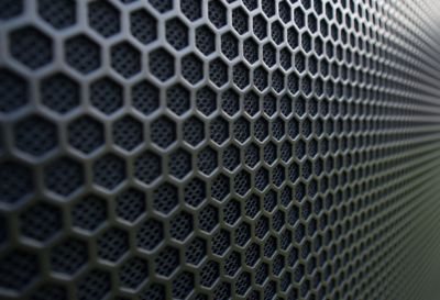Macro view of a dark metallic surface with a hexagonal perforated pattern. The depth and shadows between cells suggest durability and airflow.