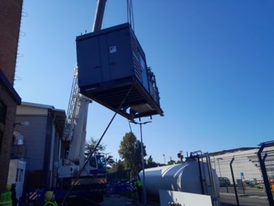 A boiler being carefully lifted into position for a district heating project, with technicians in safety gear expertly guiding the installation process.