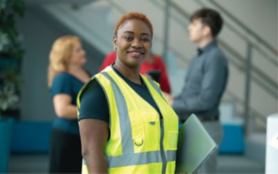 Woman employee in safety vest holding a laptop