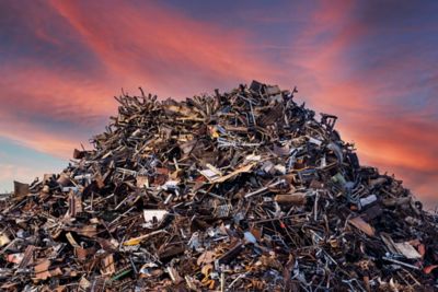 A pile of trash and metal scraps sit in a landfill under a pink and blue sunset