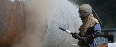 Image of man sandblasting a tank in a breathing air hood