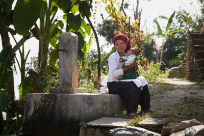 Mother with child sitting next to water pump in Nepal