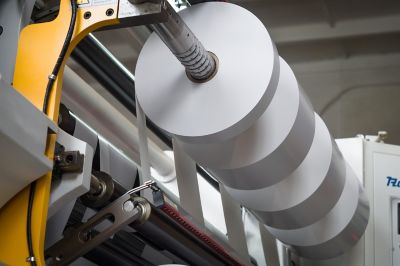 The process of winding paper self-adhesive tape into rollers of printing offer paper for printing houses. Close-up of the paper cutting and rewinding machine