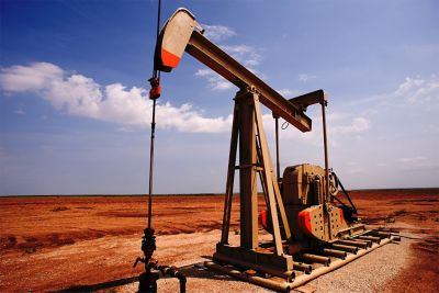 An oil well sits in an open desert, with blue sky above it