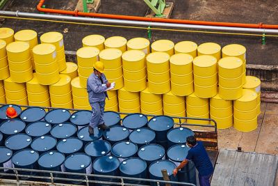 Two men are preparing to transport large barrels of oil and chemicals
