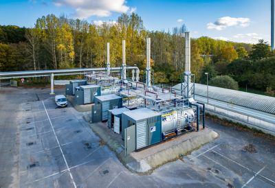 An outdoor facility showcasing multiple industrial boilers with tall chimneys, surrounded by trees at an industrial site. 