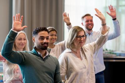 Employees raising their hands during a participative workplace session, reflecting openness and collaborative spirit