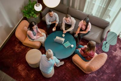 Overhead image of employees gathered around a round table in a relaxed work environment, exchanging thoughts over coffee 