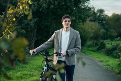 A man is walking beside his bike on a woodland path.  ​