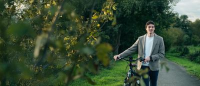 A man is walking beside his bike on a woodland path.  ​