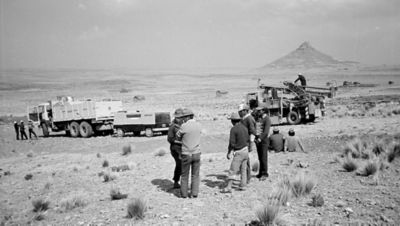 Black and white photo of equipment in Peru, with people standing around it.