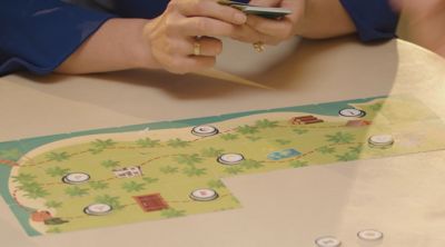 Hands holding playing cards next to board game setup.