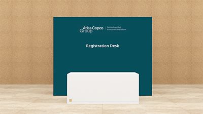 Reception desk branding with Atlas Copco Group logotype on teal backdrop, white desk in front 