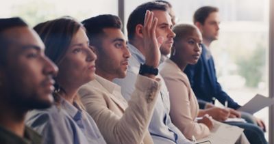 A man in an audience row has raised is hand, seemingly wanting to say something.