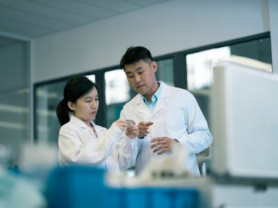 Technician in white lab coats inspecting a small item in the laboratory