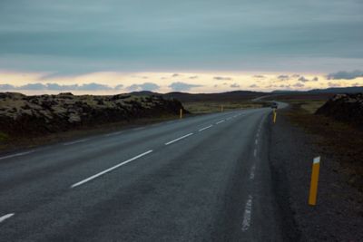 Long empty road leading through a rugged landscape under fading daylight.