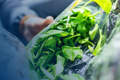 A hand holding an open bag of salad greens