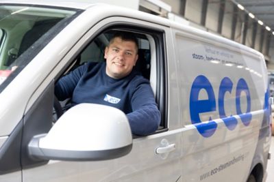 Een lachende man zit in de bestuurdersstoel van een servicebusje met ECO-label.