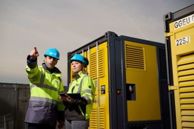 Deux travailleurs en gilets de sécurité et casques bleus se tiennent à côté des compresseurs ; l’un pointe tandis que l’autre tient une tablette.