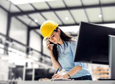 산업 현장에서 헬멧을 착용하고 데스크에서 업무 중인 여성 엔지니어 – 생산 공정 데이터 관리