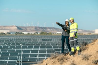 Technicians looking ahead in front of field of solar panels with wind turbines in the background