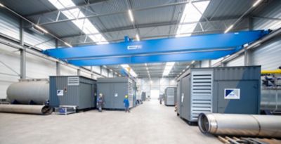 Een groot industrieel magazijn met een blauwe bovenloopkraan met diverse stoom- en warmwaterketels van Eco Steam and Heating