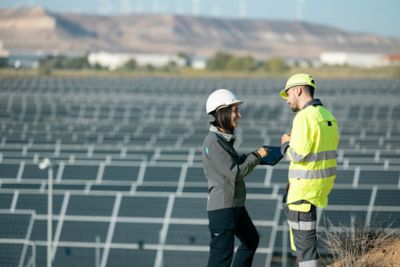 Technicians in conversation in front of field of solar panels