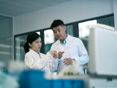 A man and woman in lab coats with focused looks on their faces working on something together.​